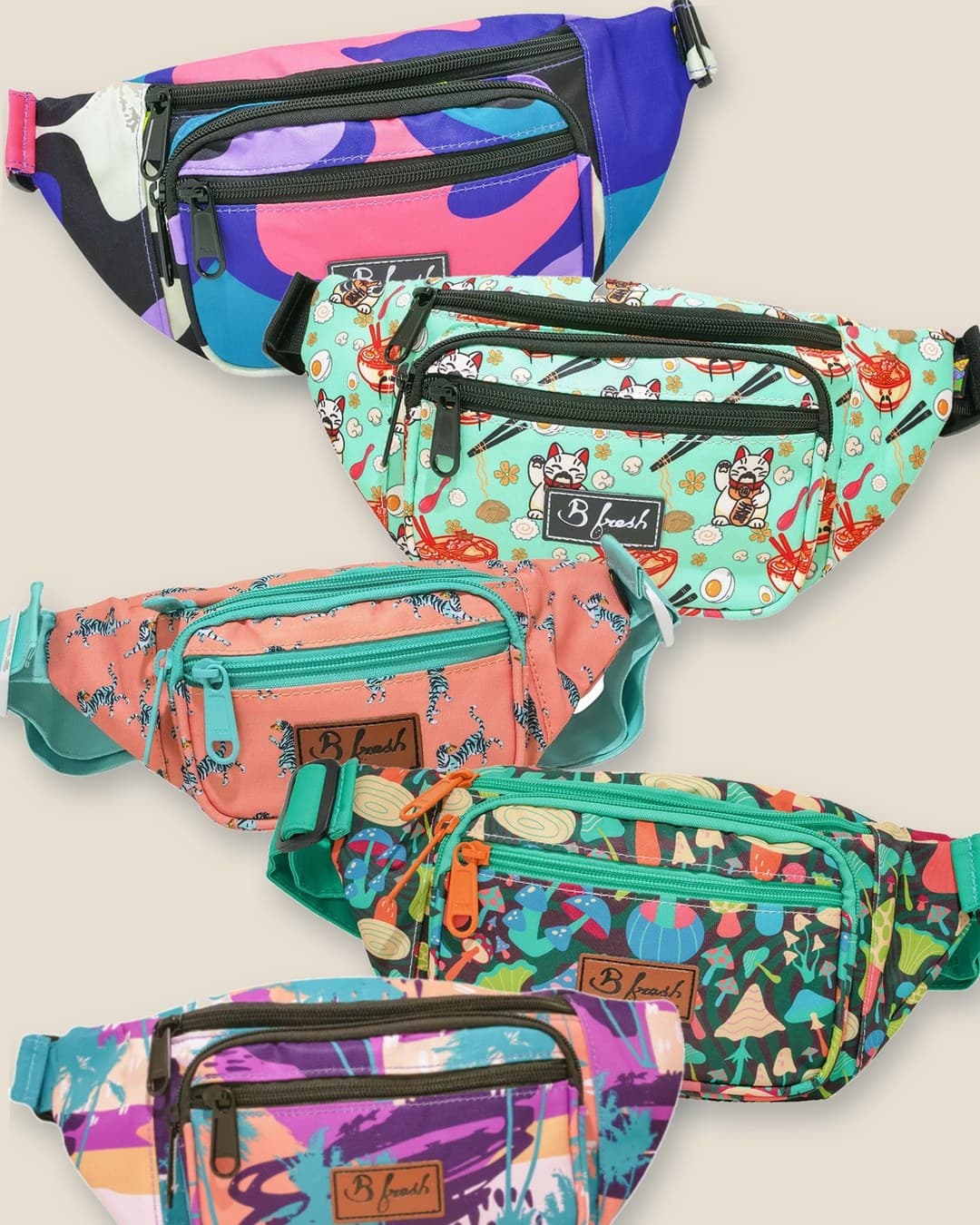 Five B Fresh Gear fanny packs in bold prints, overlapping on a warm sand background